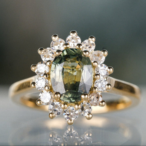 Gold ring with a green gemstone and diamond accents on a reflective surface.