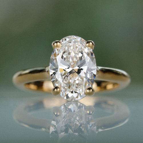 Gold ring with a diamond on a reflective surface with a blurred green background