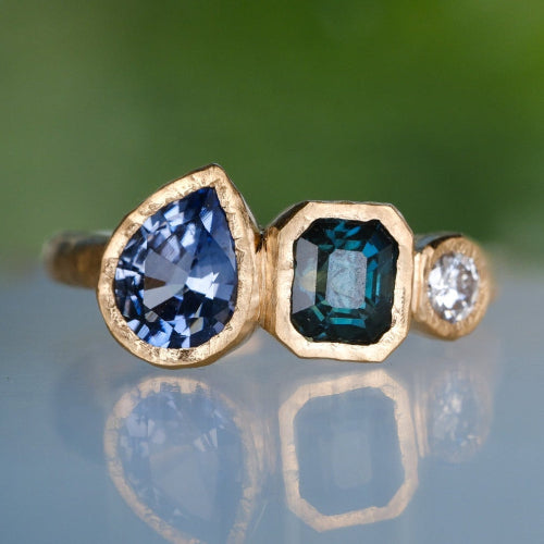 Gold ring with blue gemstones on a reflective surface with a blurred green background