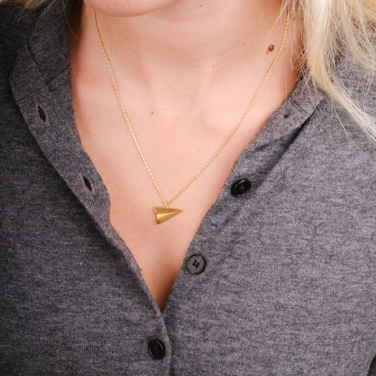 EC One gold plated recycled silver paper plane pendant necklace worn on a delicate chain against a grey shirt