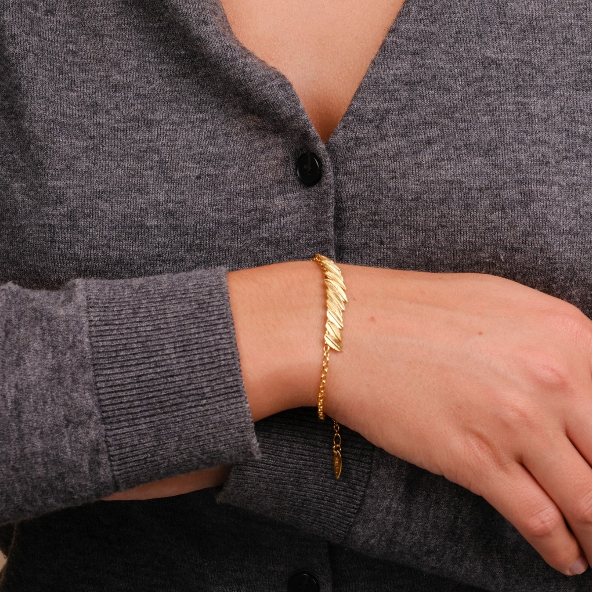 EC One gold plated Phoenix Plume bracelet worn on a wrist, featuring a delicate chain and textured feather design.