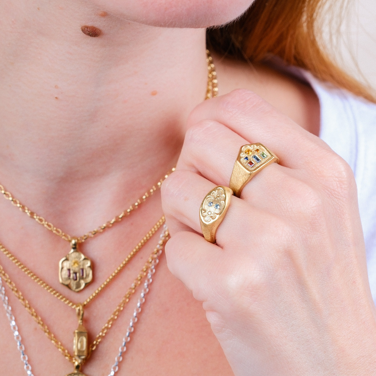 EC One gold plated ring with three mixed gemstones worn on a hand alongside a matching signet ring and necklaces