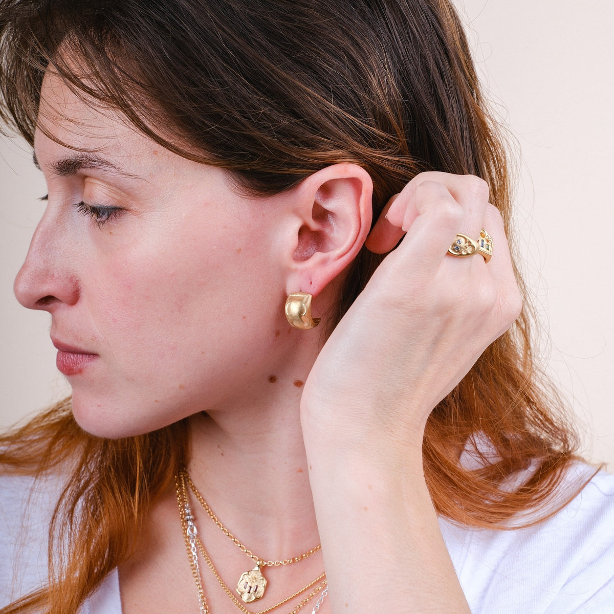 EC One medium wide gold plated hoop earrings worn by a woman with a matching ring and layered necklaces