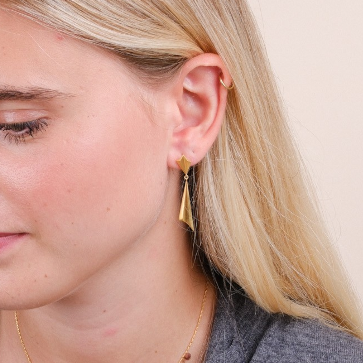 EC One gold plated pleated drop earrings worn by a blonde woman in a grey cardigan