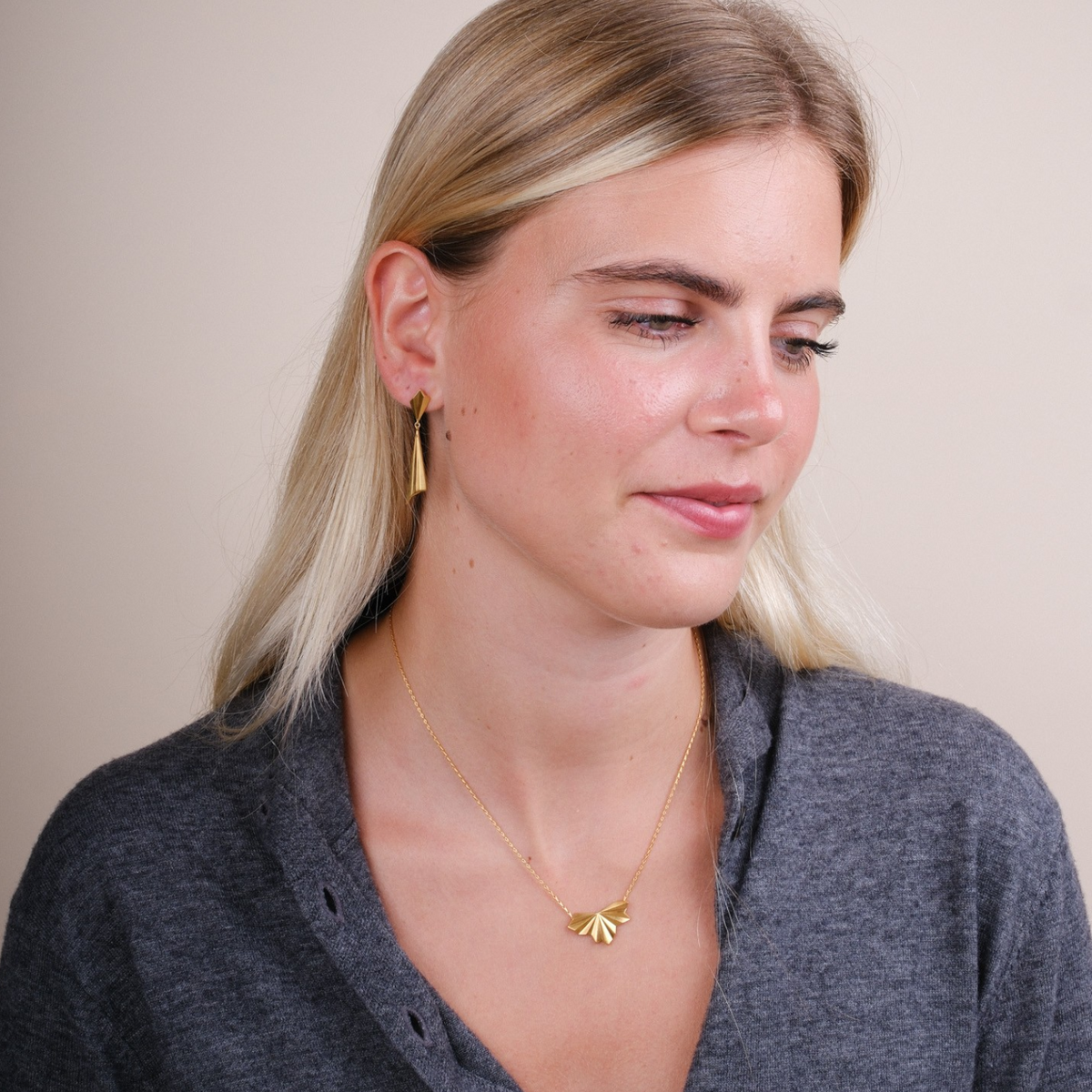 EC One gold plated pleated fan pendant necklace on a model wearing a grey top with matching fan earrings