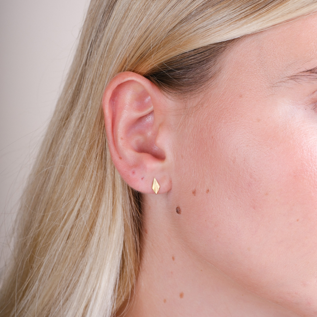 EC One tiny pleated stud earrings in gold plated recycled silver worn on a model's earlobe
