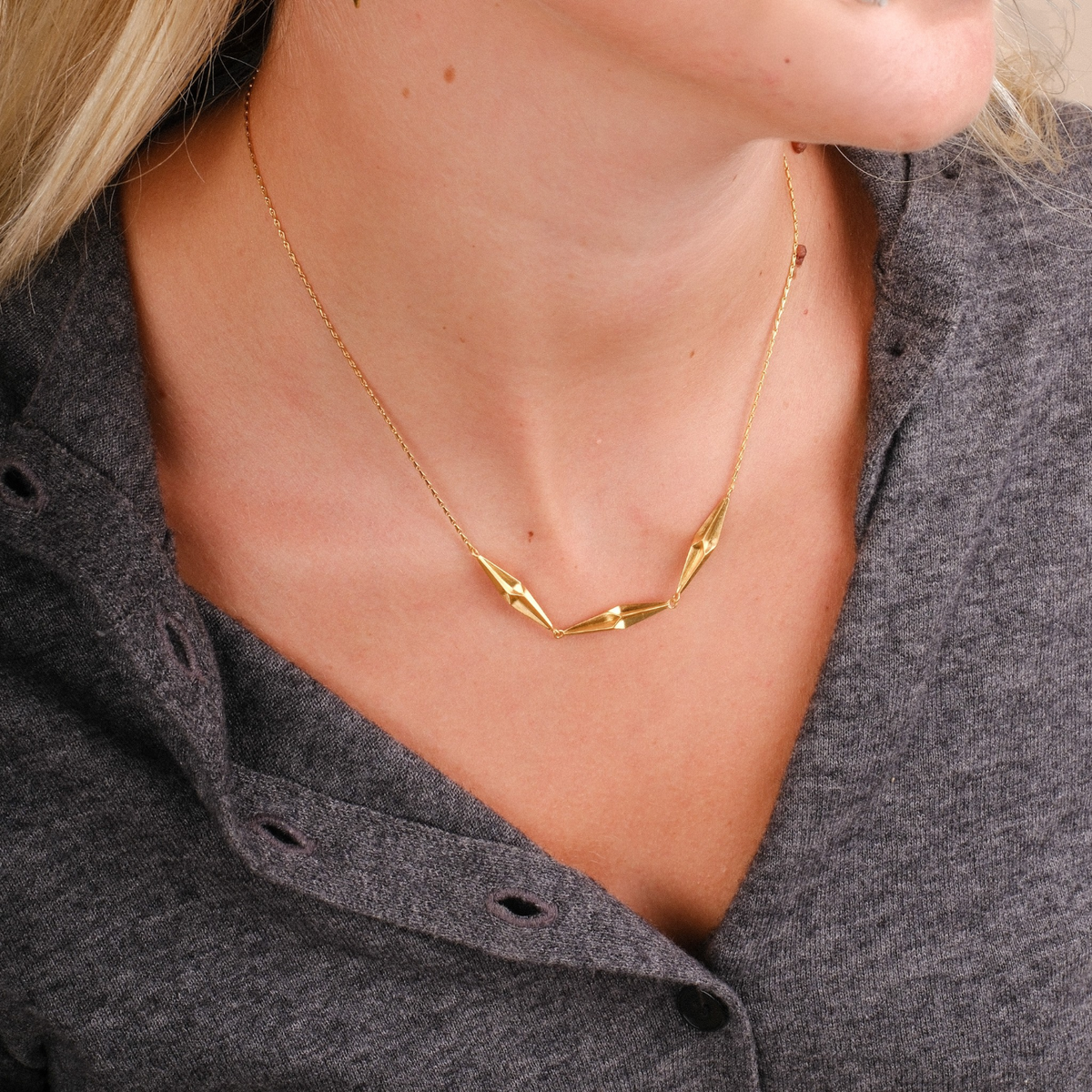 EC One gold plated recycled silver triple shard in-line necklace worn on a model with a grey collared shirt.