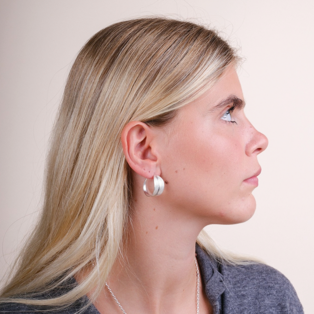 Model wearing EC One Phoenix medium silver hoop earrings, shown in profile against a neutral background.
