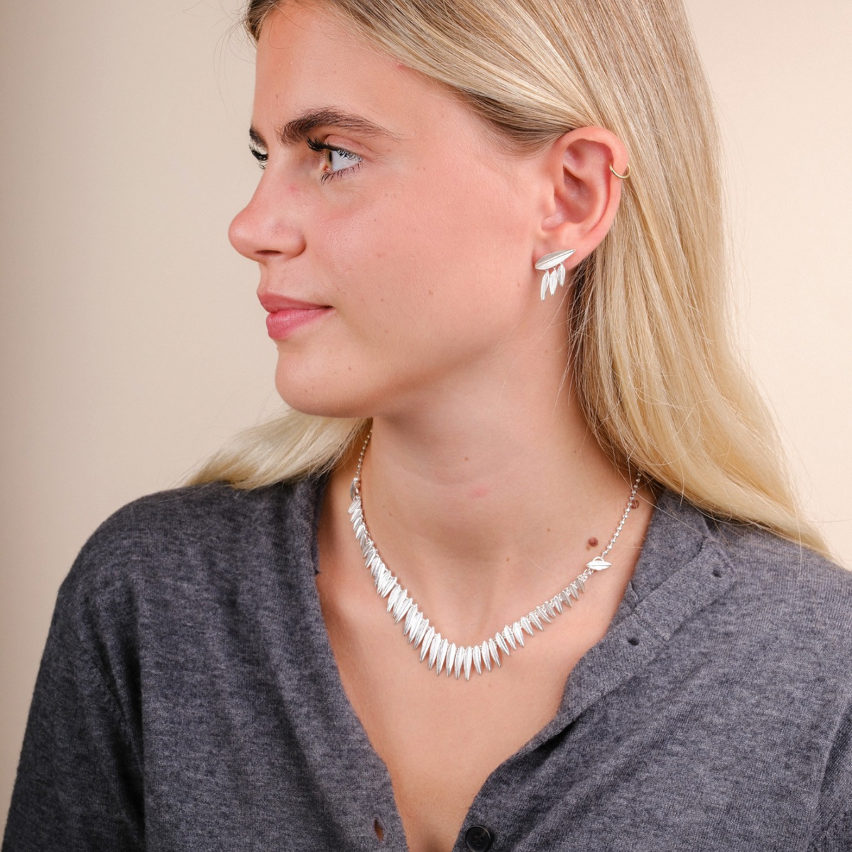Model wearing EC One silver Phoenix necklace and matching feather-style earrings against a neutral background