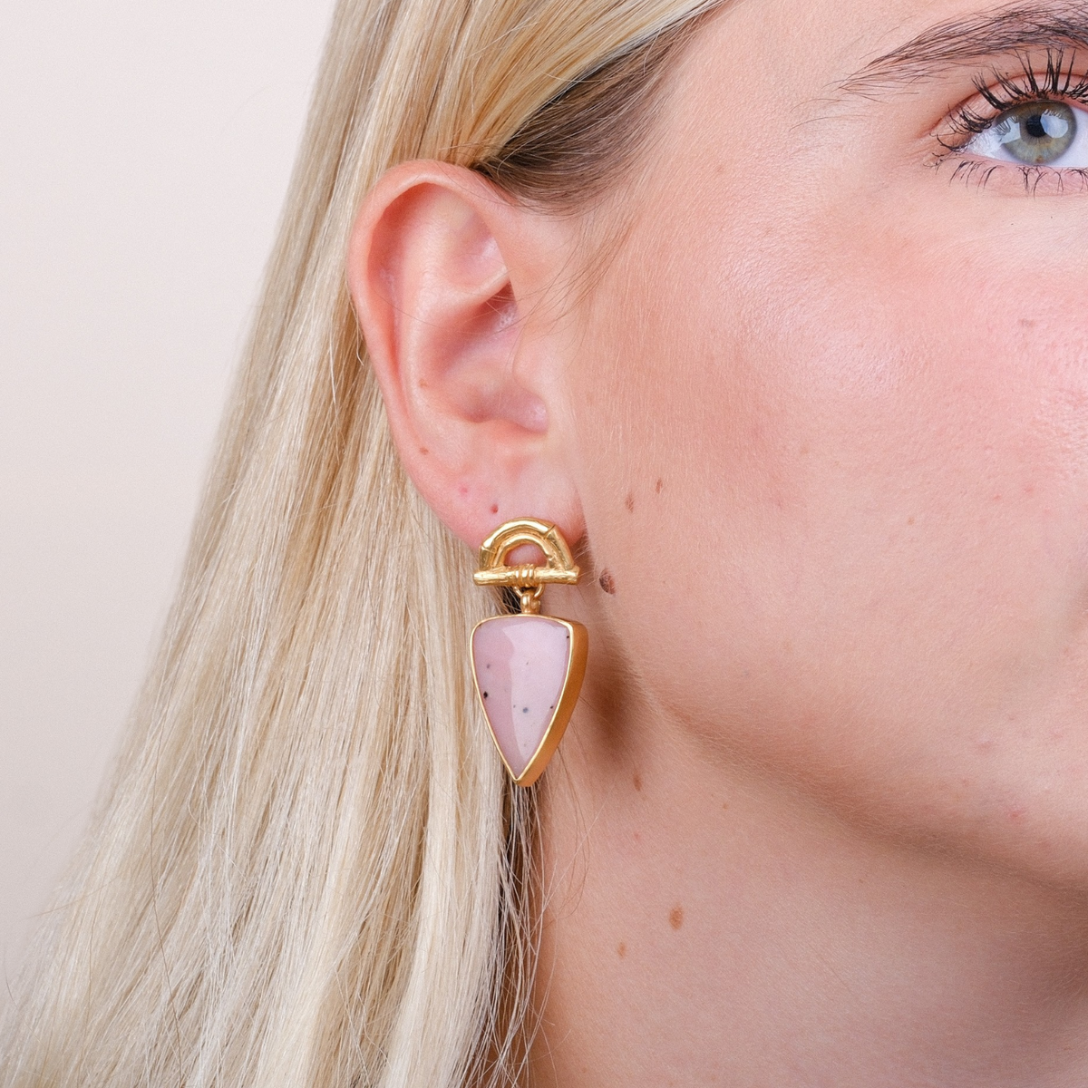 EC One Rosita Bonita gold plated bamboo arch stud earrings featuring pear-shaped pink opal gemstones on a model.