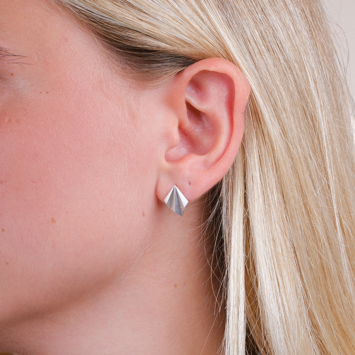 EC One Pleated stud earrings in recycled silver featuring an angular peaked design worn on a woman's ear