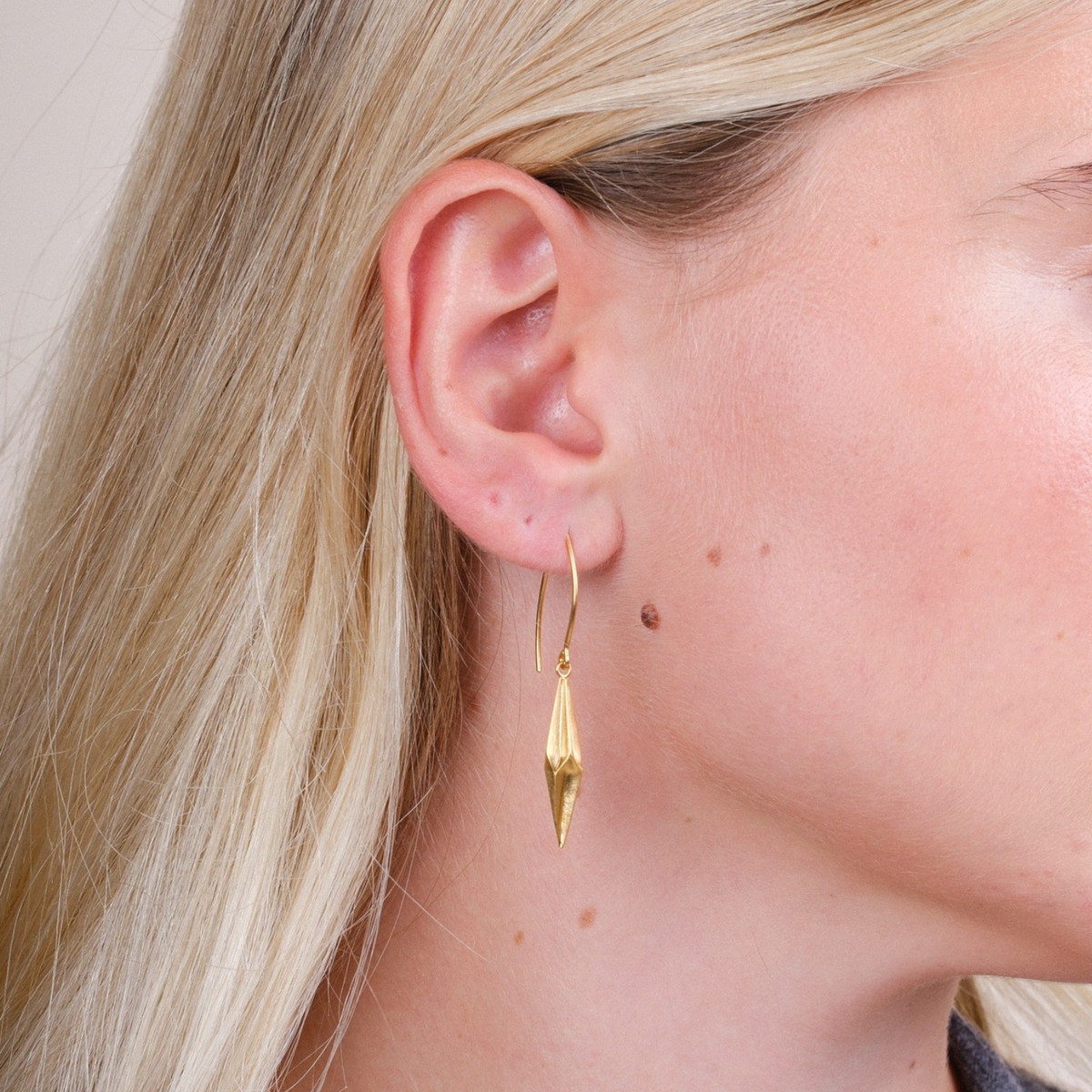 EC One Shard pleated gold-plated recycled silver drop earrings worn by a model with blonde hair.