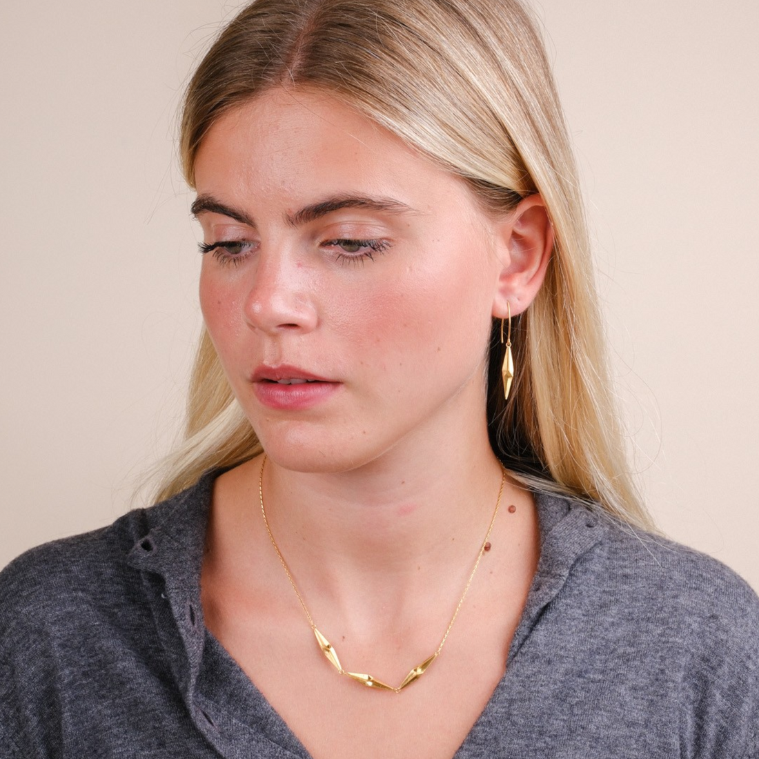 EC One Shard pleated gold plated silver drop earrings worn by a blonde woman in a grey sweater