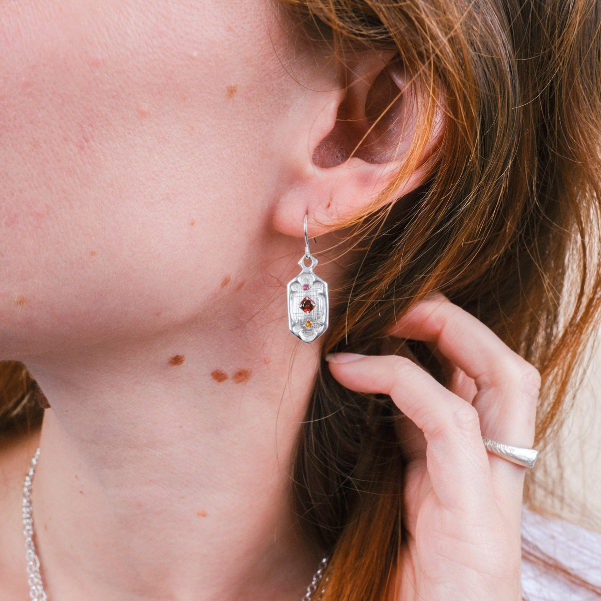 EC One silver drop earrings featuring a hexagonal window design with autumnal gemstones worn by a woman
