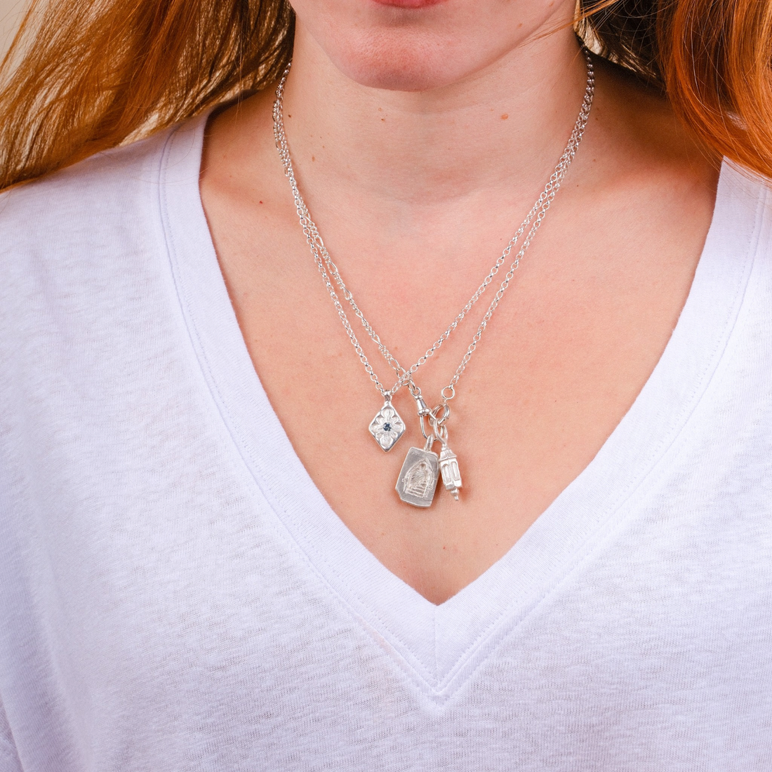 EC One silver lozenge pendant necklace with sapphire detail worn on a model in a white v-neck shirt