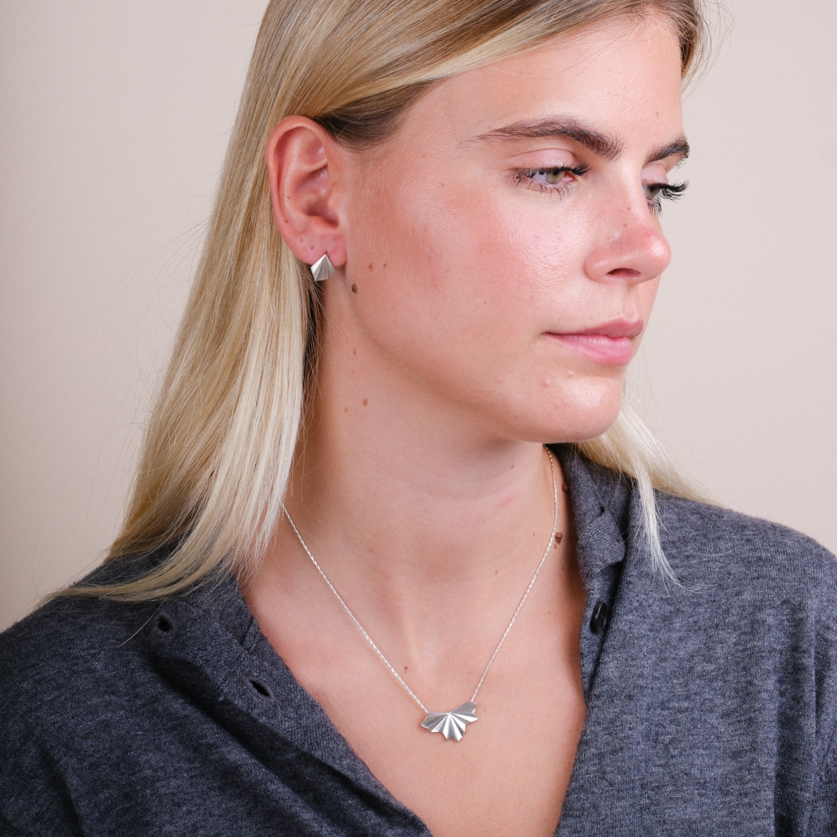 EC One silver pleated fan pendant necklace on a model wearing a grey top, featuring an adjustable hayseed chain.