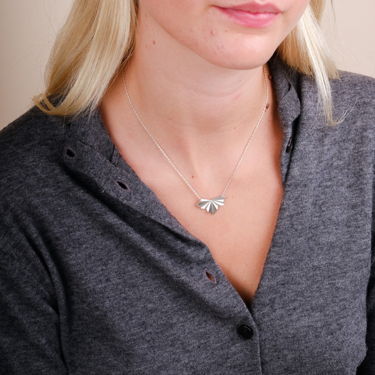EC One silver pleated fan pendant necklace on a delicate hayseed chain worn by a model in a grey button-up shirt.
